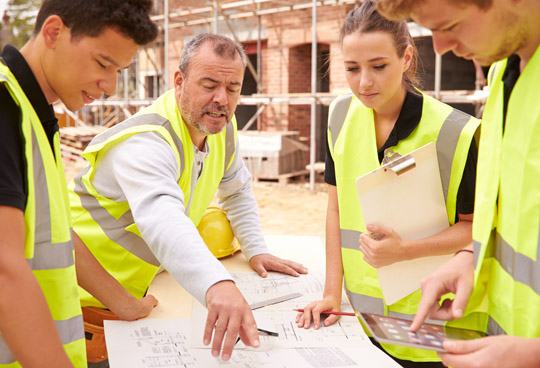 Team members discuss project while overlooking plans